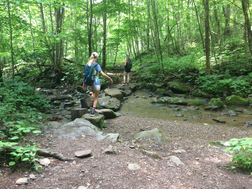 Two women cross creek on stepping stones at South River Falls trail in Shenandoah National Park