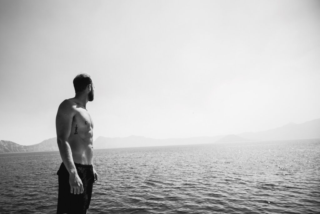fit man without shirt looking over water with mountains in background