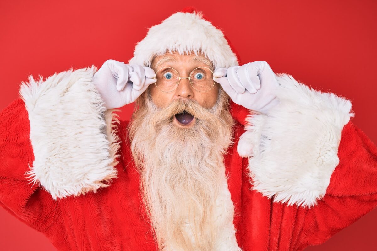 a surprised Santa Claus adjusting his glasses. A red background is behind him.