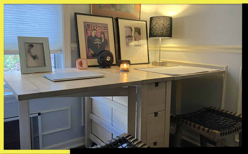 a writing desk with a window view. On top we see a framed photo, a timer, and a lamp lighting up the corner of a room